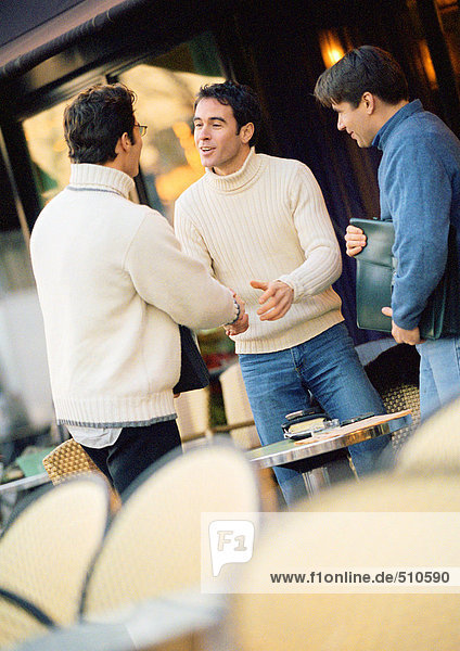 Drei Männer auf der Caféterrasse  zwei schüttelnde Hände.