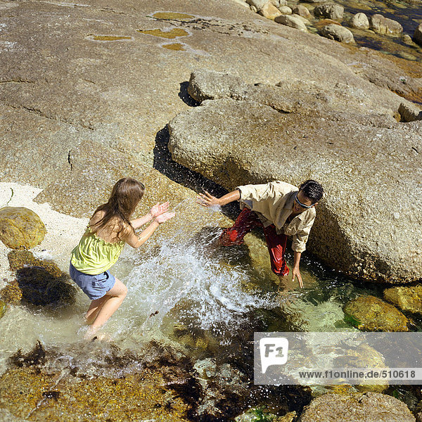 Teenage boy and little girl splashing in water  high angle view