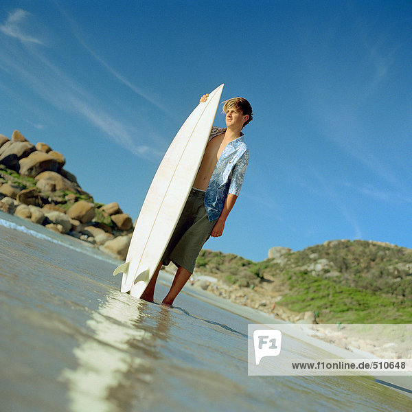 Junge im flachen Wasser stehend mit Surfbrett