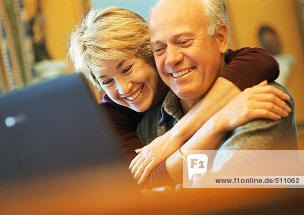 Mature couple smiling  man using laptop  woman with arms around man
