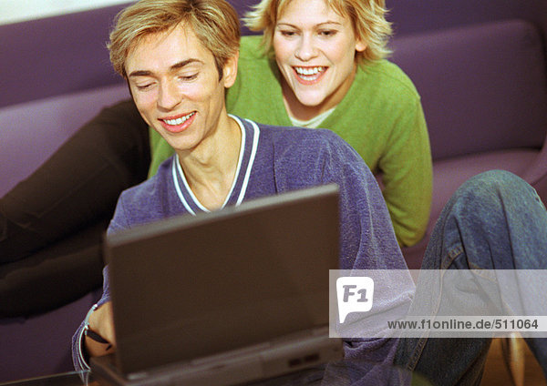Couple smiling  man using laptop  woman sitting  looking over man's shoulder.