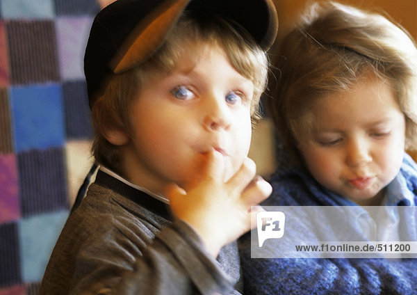 Zwei Kinder  eines schaut mit dem Finger im Mund in die Kamera  verschwommen.