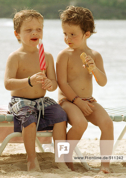 Zwei Kinder essen Eis am Strand.