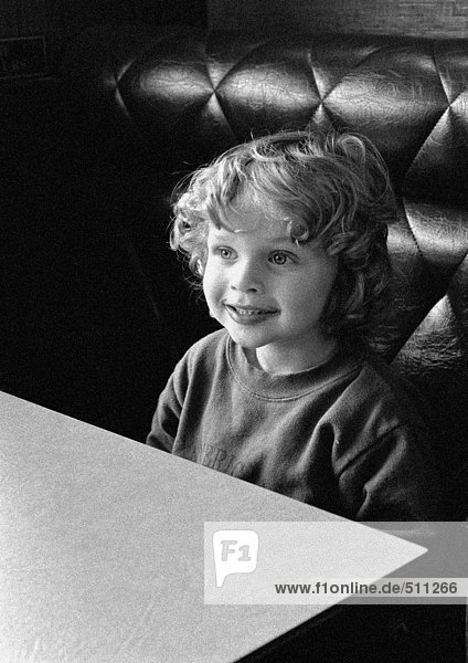 Kind am Tisch sitzend lächelnd  Portrait  s/w.