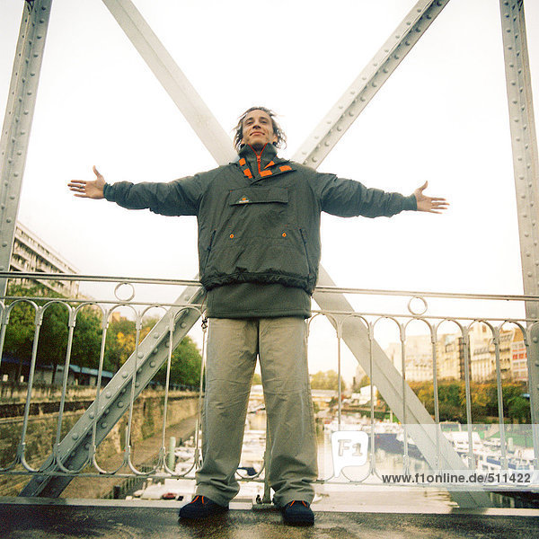 Man standing on bridge wearing winter clothes with arms stretched out