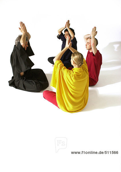 Gruppe von Menschen  die auf dem Boden sitzen und mit den Händen über dem Kopf meditieren.