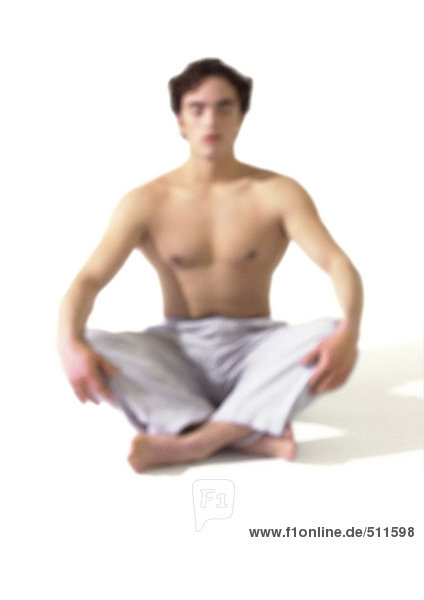 Oben-ohne-Mann auf dem Boden sitzend im indischen Stil,  meditierend,  verschwommen
