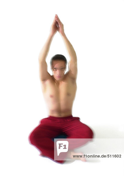 Oben-ohne-Mann auf dem Boden sitzend,  mit erhobenen Armen über dem Kopf meditierend.