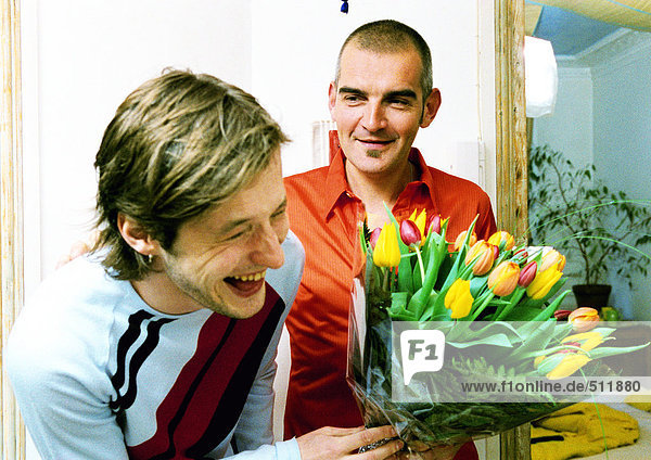 Zwei Männer lächelnd und lachend,  einer mit Blumenstrauß,  Portrait.