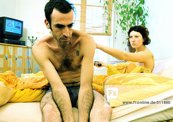 Paar im Bett  Mann sitzt halbnackt  Frau zeigt.