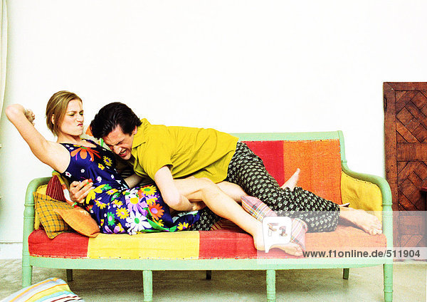 Paar auf Sofa  Mann stürzt sich auf Frau  Frau mit Arm bereit zum Schlagen