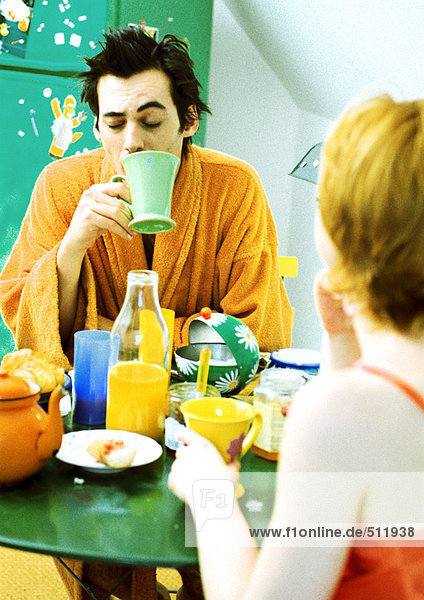 Junges Paar am Tisch beim Frühstück,  Frau in Rückansicht.