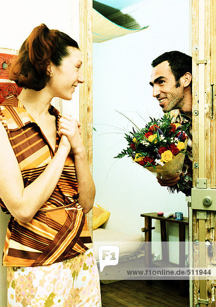 Paar  Mann geht durch die Tür und hält Blumenstrauß  Frau lächelt.