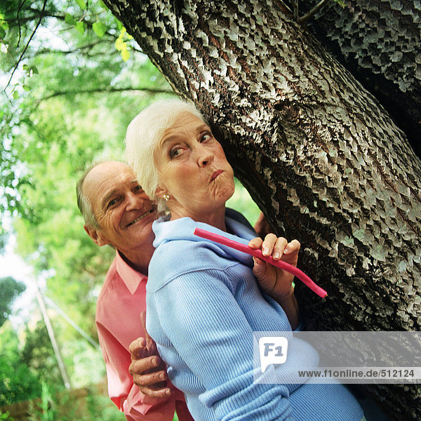 Erwachsener Mann und Frau  die hinter einem Baum stehen.