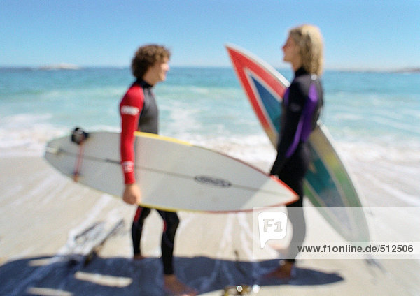 Zwei junge Männer mit Surfbrettern am Strand  die sich gegenüberstehen  verschwommen.
