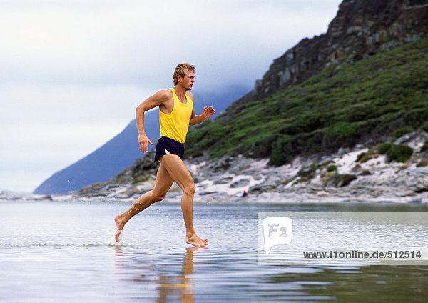 Junger Mann joggt durchs Wasser  Berge im Hintergrund.