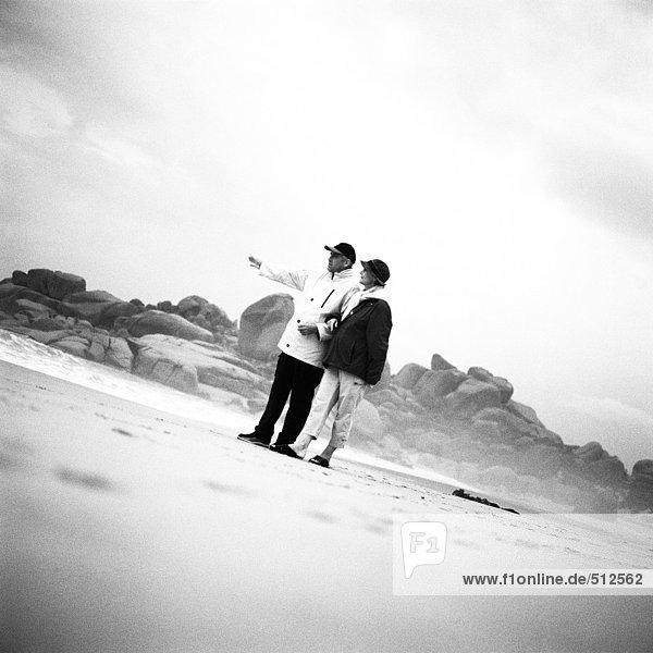Erwachsenes Paar am Strand stehend  Mann zeigt  s/w.