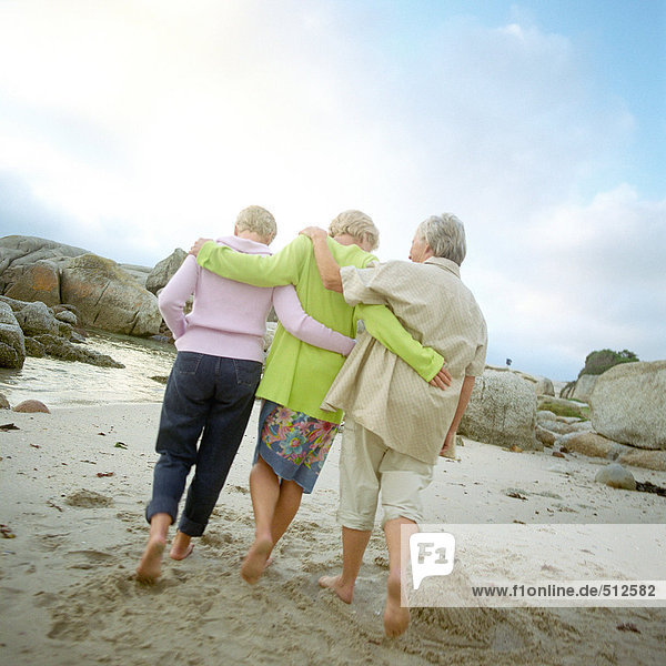 Three mature friends arm in arm  walking on beach  rear view