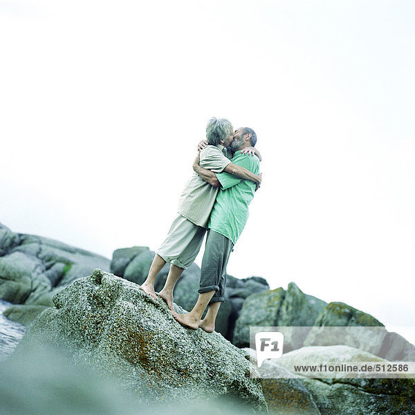 Ein reifes Paar  das sich küsst und auf Felsen steht.