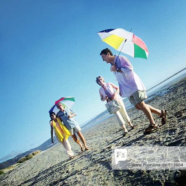 Two mature couples standing on beach  men holding umbrellas