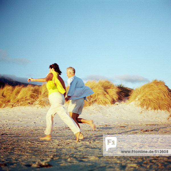 Mature couple running on beach  side view