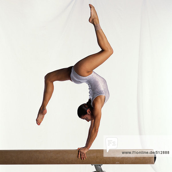 Young female gymnast on balance beam performing  side view