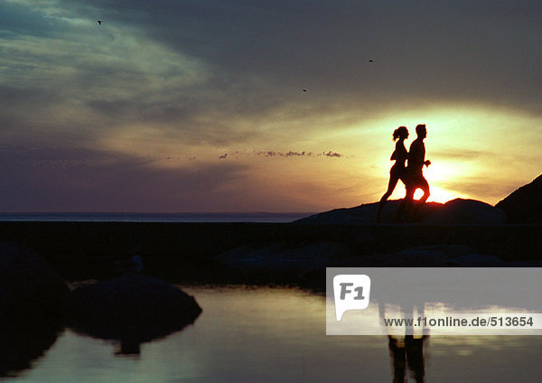 Paar läuft bei Sonnenuntergang am Wasser  Silhouette