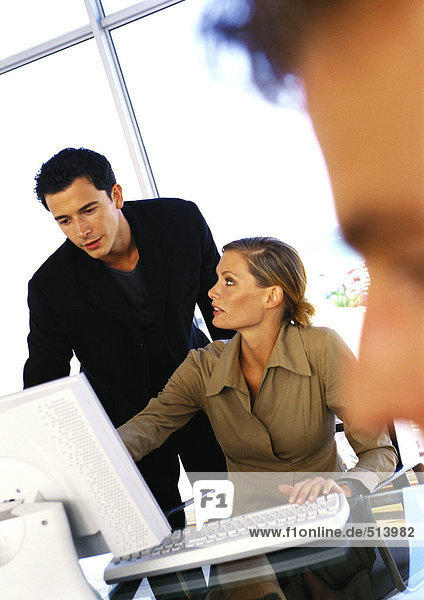 Businessman and woman using computer  second man's face blurred in foreground