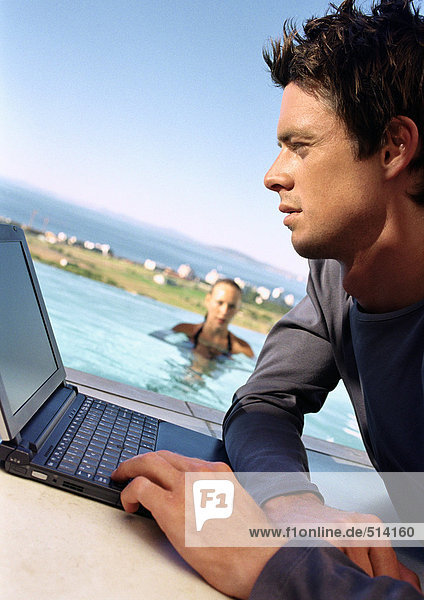 Mann mit Laptop  Frau im Schwimmbad im Hintergrund