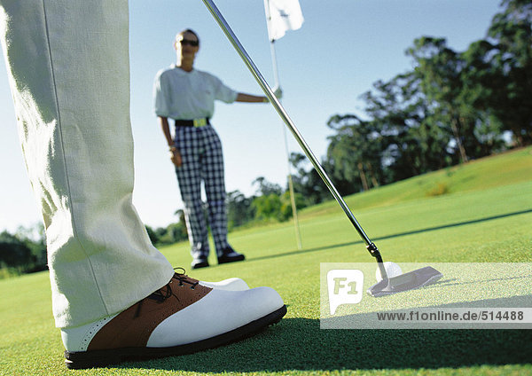 Golfer putting and second golfer holding pole