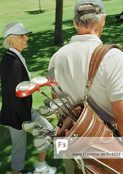 Two mature golfers  one carrying clubs  rear view