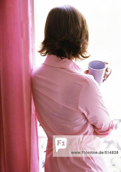 Woman holding mug  looking out window  rear view