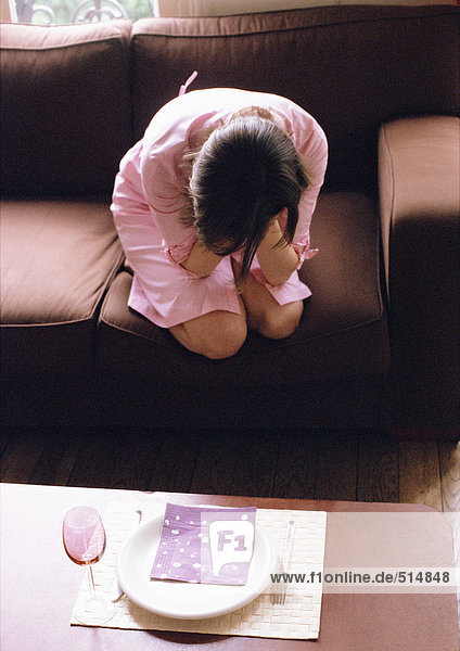 Woman kneeling on sofa  head in hands