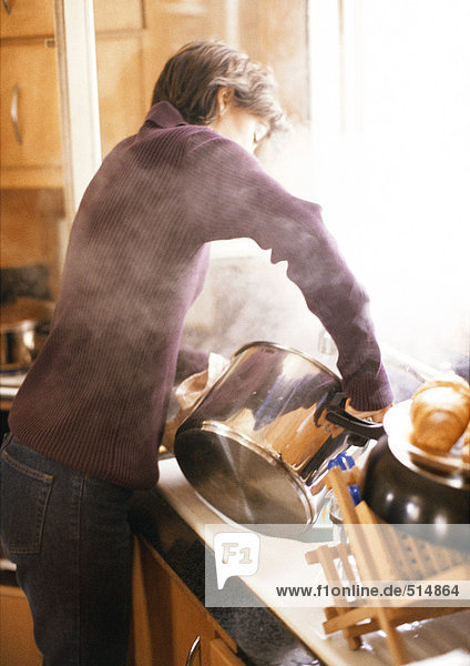 Woman holding steaming pot above sink