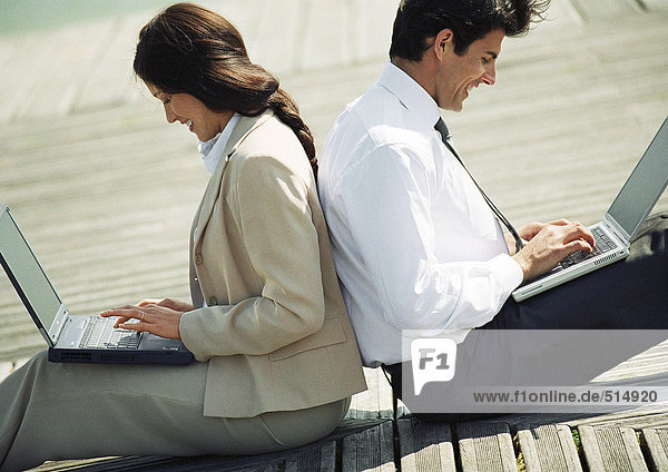 Geschäftsmann und Frau Rücken an Rücken auf dem Boden mit Laptop-Computern auf dem Schoß