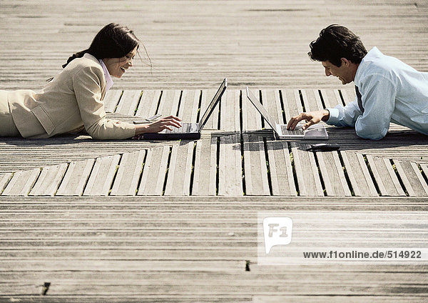 Mann und Frau auf dem Bauch liegend  im Freien  mit Laptop-Computern