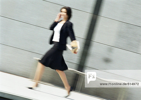 Businesswoman using cell phone and walking  blurred