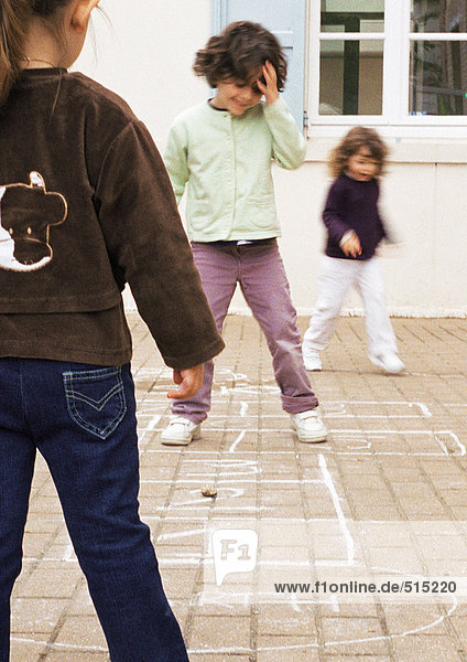 Drei Kinder spielen Hopscotch