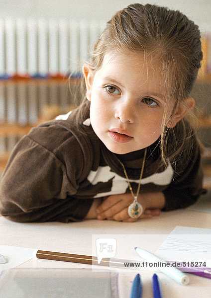 Kind sitzt am Tisch  lehnt sich nach vorne  Kopf und Schultern  Nahaufnahme