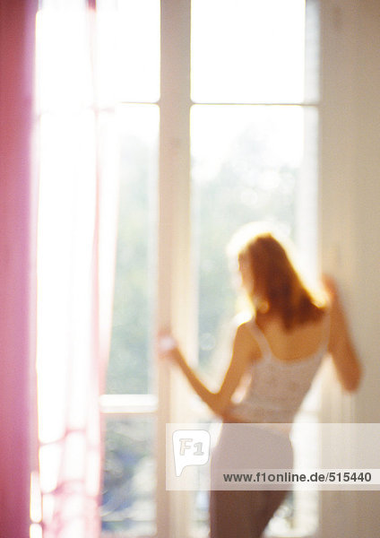 Woman looking out of window  rear view  three quarter length  blurred.