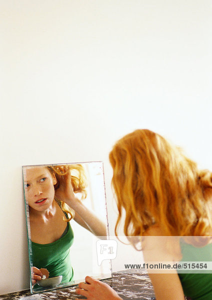 Woman looking at reflection in mirror  pulling her hair back.