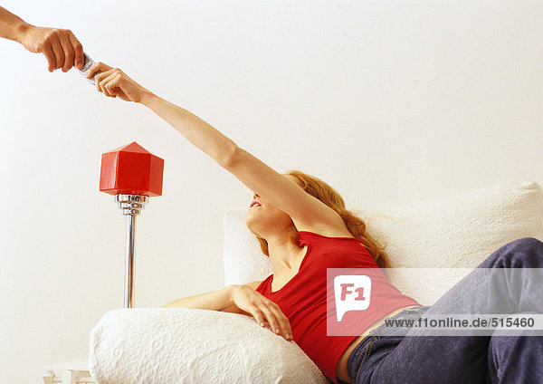 Woman on couch handing remote to someone.