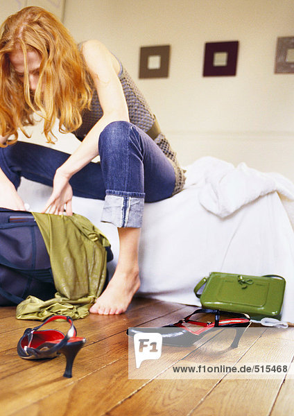 Woman sitting on bed looking through bag.