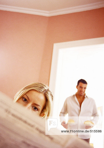 Woman reading paper  man in background holding food