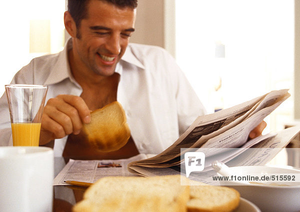 Ein Mann  der Zeitung liest und frühstückt.