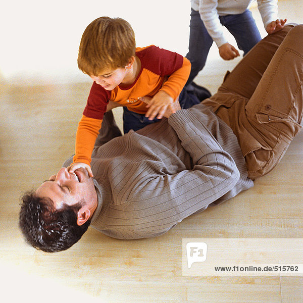 Kinder spielen mit Vater auf dem Boden