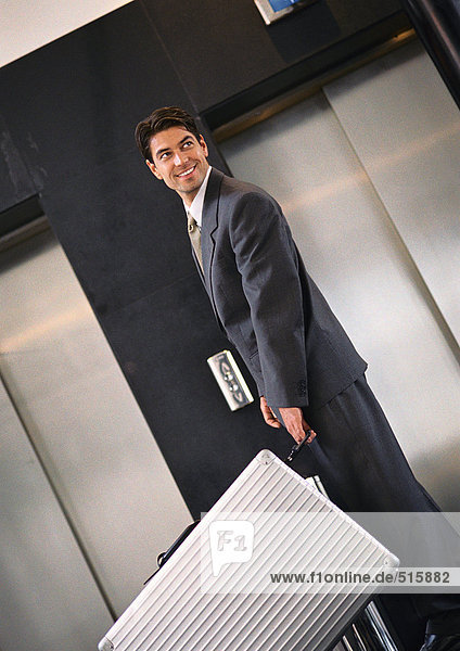 Businessman standing near elevators with suitcase  looking over shoulder