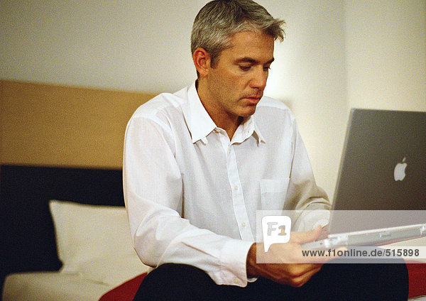 Geschäftsmann auf dem Bett sitzend mit Laptop