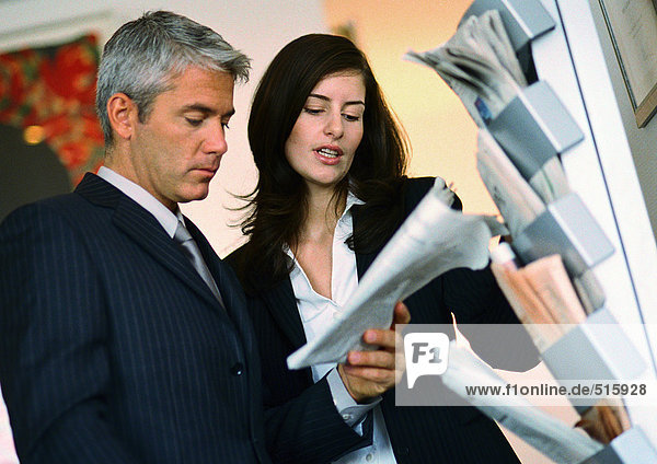 Businessman and businesswoman looking at newspaper