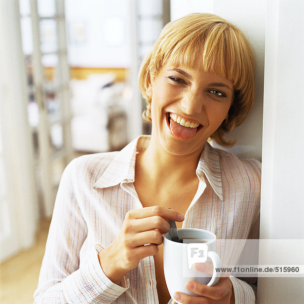 Teenagermädchen hält eine Tasse Kaffee  streckt die Zunge vor der Kamera heraus.